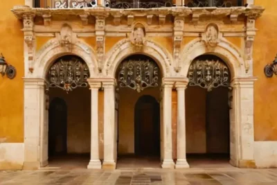 Un antiguo edificio con un revestimiento de piedra gastado y una entrada barroca se funde con el paisaje circundante en un ambiente relajante