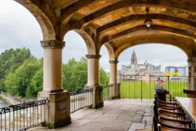 La escena describe una pintoresca plaza con características de arquitectura clásica y elementos naturales en un ambiente sombreado y tranquilo