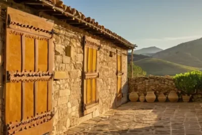 La descripción evoca una villa andaluza con casas de piedra y tejas rojas rodeadas por oliveras y cerros bajo un cielo soleado