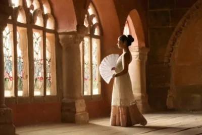 Una bailarina tradicional está en escena entre arcos de piedra iluminados por débiles colores a través de ventanas manchadas