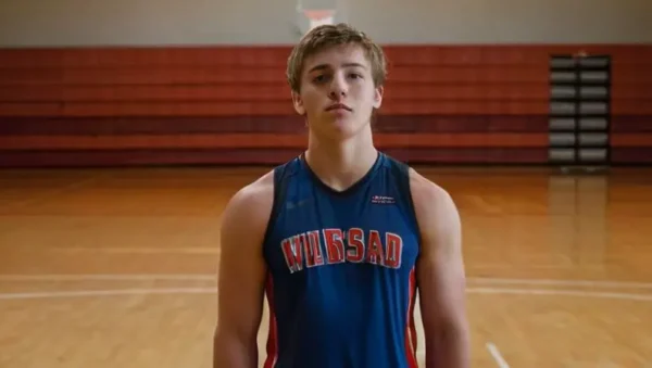 Un joven jugador de baloncesto se encuentra en medio de una gimnasio iluminada con fluorescencia