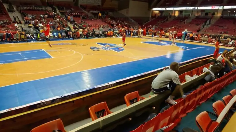 Un gimnasio olvidado muestra un equipo juvenil ansioso y listo para jugar un partido de baloncesto bajo la luz débil e indirecta de los focos