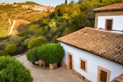 El escenario es una pintoresca aldea mediterránea con casas de terracota y tejados cubiertos de musgo en un paisaje ondulado