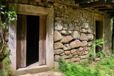 Un edificio de una mina antigua se yergue entre la vegetación exuberante del bosque español con paredes desgastadas y una puerta de madera que cuelga torpemente