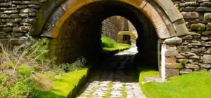 Un niño contempla la arquitectura del puente romano con detalles como piedras erosionadas y crecimientos de musgo